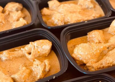 A group of containers filled with chicken in a curry sauce.